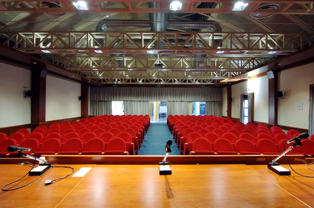 La sala conferenze vista dal palco, con le poltroncine rosse e la regia in fondo